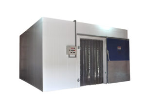 a câmara fria tem um formato retangular e é feita de metal na cor branca. A porta está aberta para a direita e sua parte interna é nas cores cinza e azul. A abertura conta com fitas plásticas que vão do teto até o chão e ao seu lado, na esquerda, está o painel de controle com botões coloridos.