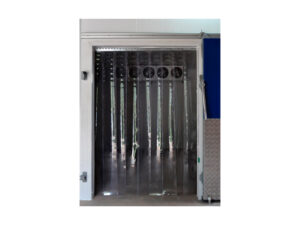 Imagem da cortina de PVC instalada na abertura de uma câmara fria. As tiras flexíveis são transparentes e se estendem do teto até o piso. Ao fundo é possível ver a entrada de ar da câmara fria e na parte direita da foto um pedaço da porta, nas cores azul e cinza.