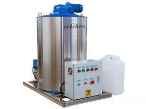 A imagem mostra o gerador de gelo em escama/flocos. Ele possui um grande tambor prateado, com topo azul e quadro elétrico com botões vermelhos e verdes. O fundo da imagem é branco.