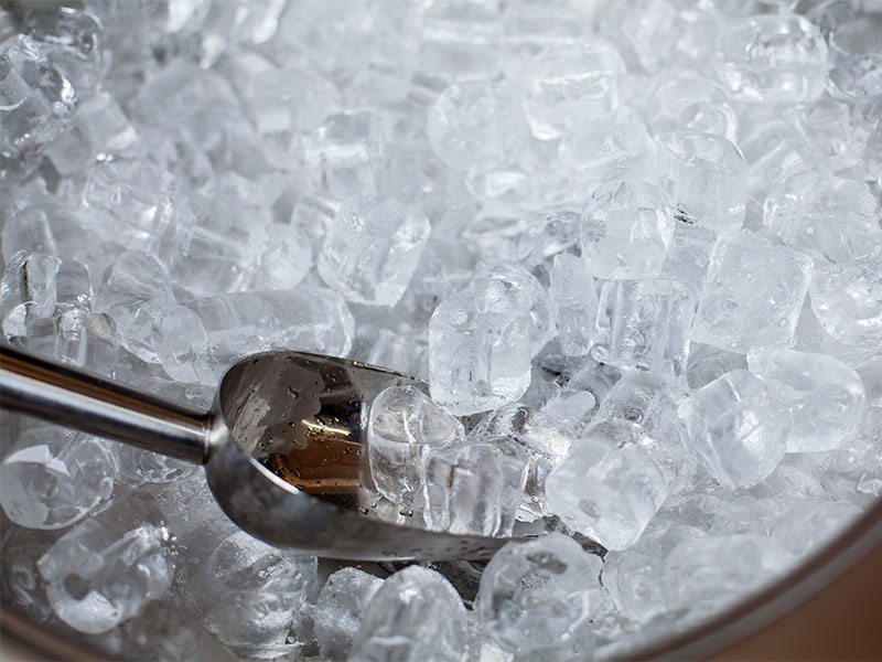 A imagem mostra um recipiente redondo preenchido com gelo em tubos. À esquerda está uma pá de gelo, com uma pequena porção dentro dela.