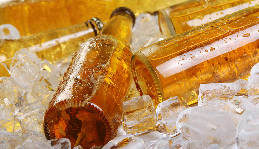 Na imagem há cinco garrafas marrons de cerveja. Elas estão dentro de um recipiente com gelo em tubos.